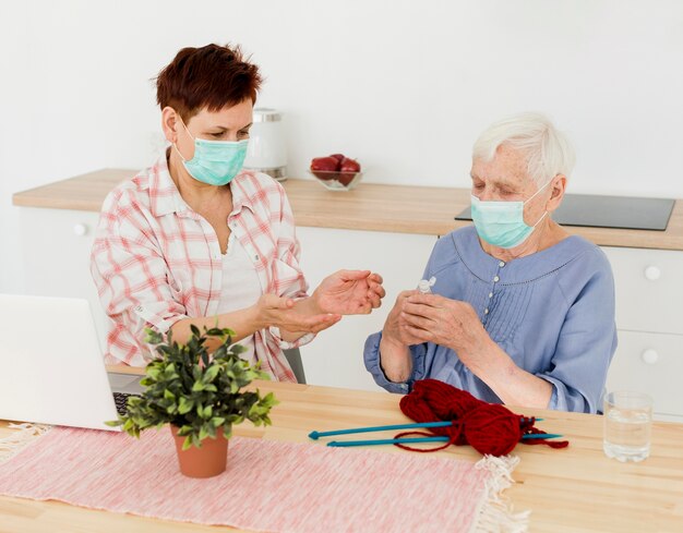 Mujeres mayores con máscaras médicas que desinfectan sus manos mientras tejen
