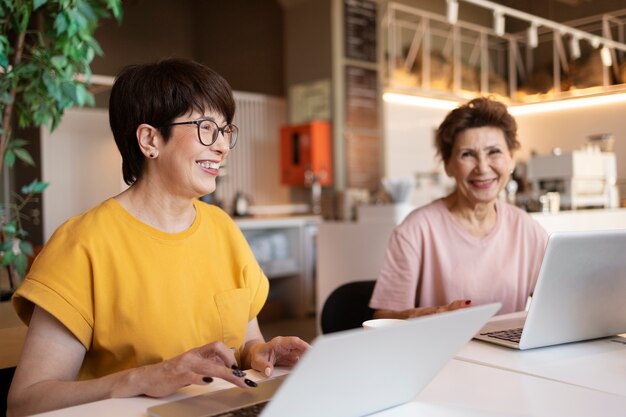 Mujeres mayores que pasan tiempo juntas en un café y trabajan en sus computadoras portátiles