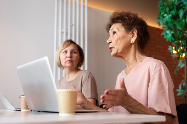 Mujeres mayores que pasan tiempo juntas hablando y trabajando en una computadora portátil