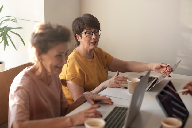 Mujeres mayores que pasan tiempo juntas y trabajan en sus computadoras portátiles