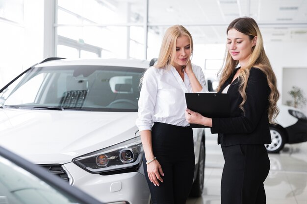 Mujeres mirando portapapeles en concesionario de automóviles