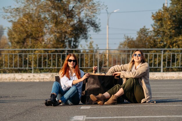 Mujeres de moda joven con bolsas de la compra sentado en el estacionamiento