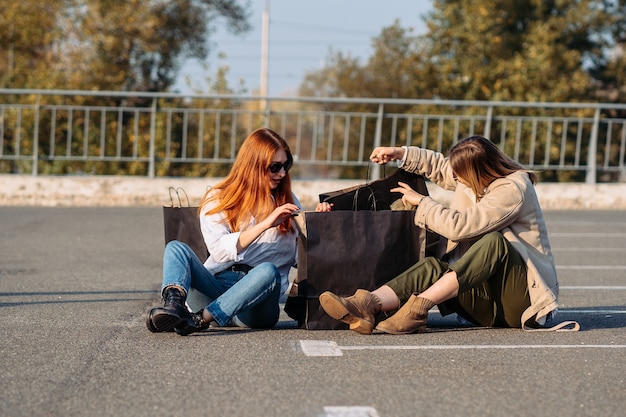 Mujeres de moda joven con bolsas de compras sentado en el estacionamiento