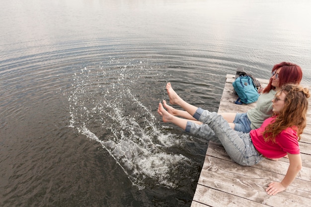 Foto gratuita mujeres en el muelle y salpicando agua con los pies +