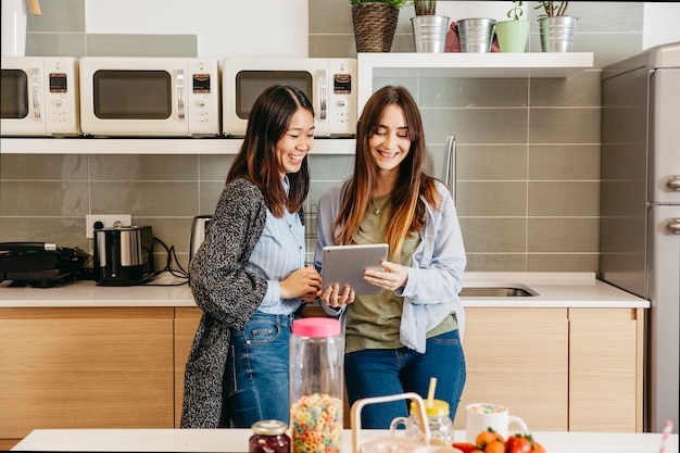 Mujeres multiétnicas alegres con tableta en la cocina