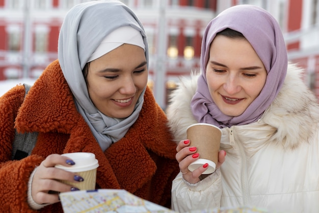 Foto gratuita mujeres musulmanas con hijabs bebiendo café y consultando un mapa mientras están de vacaciones