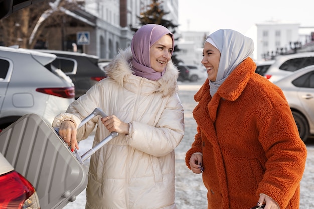 Mujeres musulmanas con hijabs sacando su equipaje del maletero de un coche mientras están de vacaciones