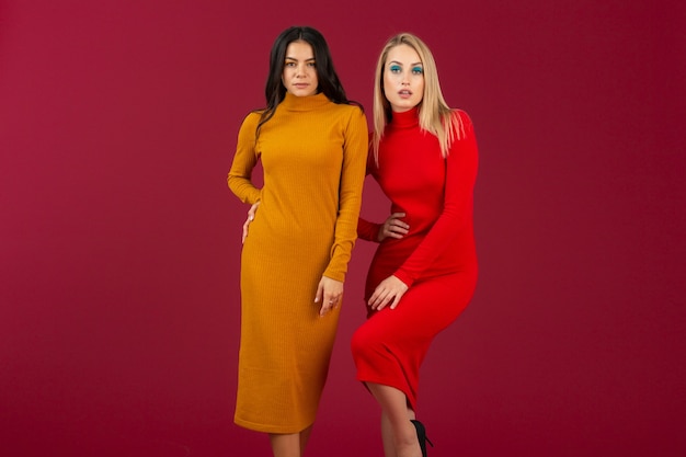 Mujeres muy elegantes en vestido de punto de moda otoño invierno amarillo y rojo posando aislado en la pared roja