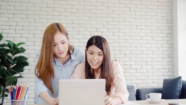 Mujeres de negocios asiáticas creativas inteligentes atractivas en la ropa de sport elegante que trabaja en el ordenador portátil mientras que se sienta