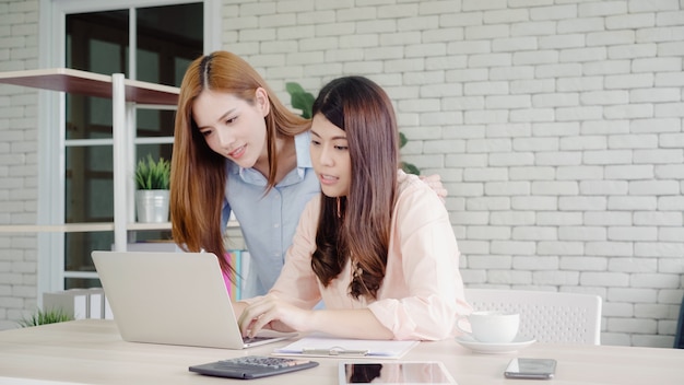 Mujeres de negocios asiáticas creativas inteligentes atractivas en la ropa de sport elegante que trabaja en el ordenador portátil mientras que se sienta