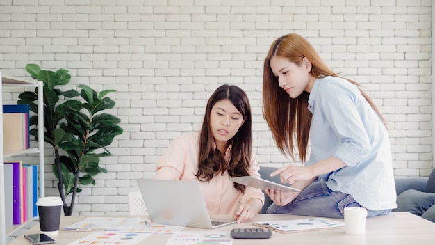 Mujeres de negocios asiáticas creativas inteligentes atractivas en la ropa de sport elegante que trabaja en el ordenador portátil mientras que se sienta