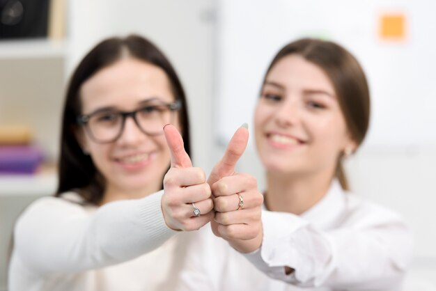 Mujeres de negocios jovenes borrosas que muestran el pulgar encima de la muestra hacia cámara