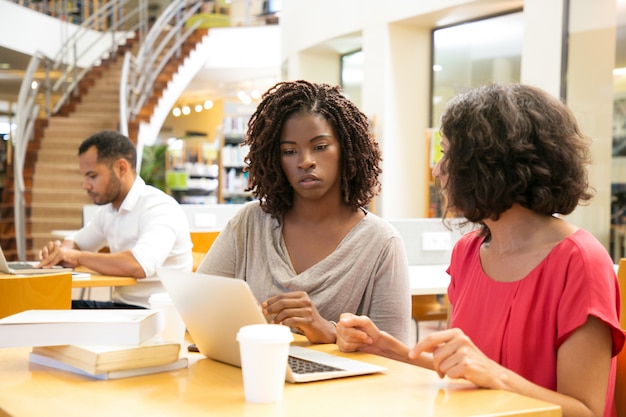 Mujeres pensativas que usan la computadora portátil en la biblioteca