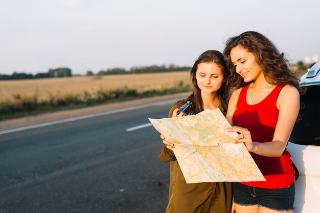 Mujeres de pie cerca de coche blanco y mirando el mapa