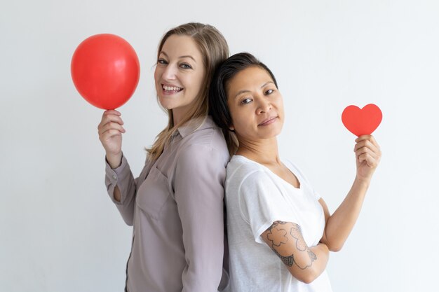 Mujeres de pie espalda con espalda con globo rojo y corazón de papel.