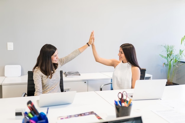 Foto gratuita mujeres profesionales sonrientes chocando los cinco después de completar tareas en el escritorio en el lugar de trabajo