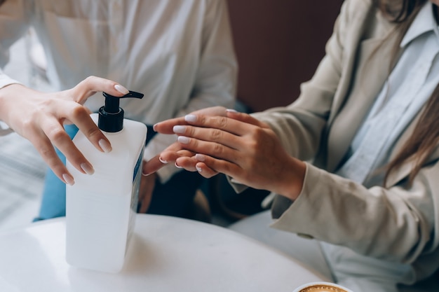 Mujeres que usan un antiséptico antibacteriano para desinfectar en el café. Nuevas reglas sociales tras el concepto de pandemia.