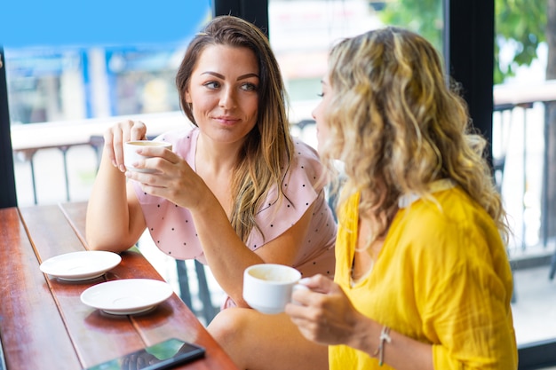 Mujeres relajadas charlando y tomando café en la cafetería