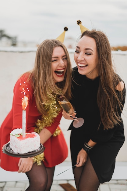 Mujeres riendo en vestidos rojos y negros sosteniendo la tarta de cumpleaños y la copa de champán