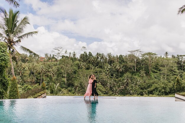 Mujeres románticas en vestidos largos posando en la hermosa naturaleza. Foto de cuerpo entero al aire libre de mujeres que pasan tiempo en el resort.