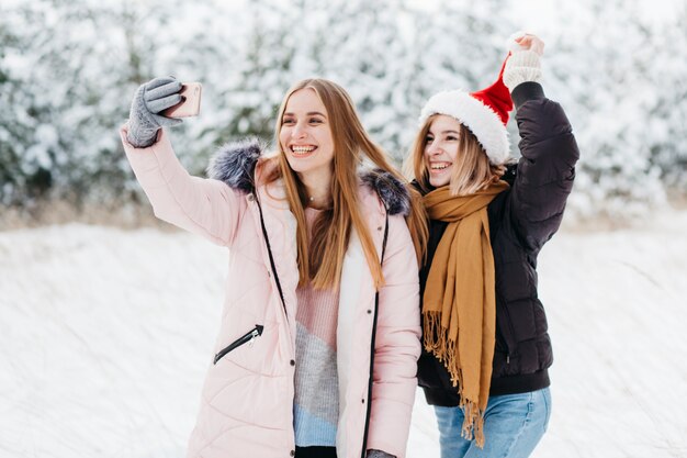 Mujeres en Santa sombrero tomando selfie en bosque de invierno