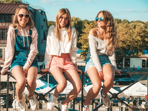 Mujeres sexy sentadas en pasamanos en la calle. Modelos positivos divirtiéndose en gafas de sol. Comunicando y discutiendo algo