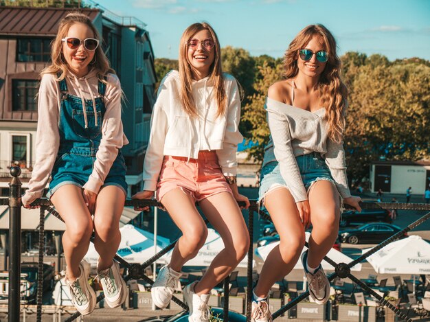 Mujeres sexy sentadas en pasamanos en la calle. Modelos positivos divirtiéndose en gafas de sol. Comunicando y discutiendo algo