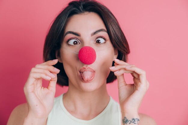 Mujeres sobre fondo rosa mujer joven muy divertida y sonriente con nariz de payaso, humor de fiesta