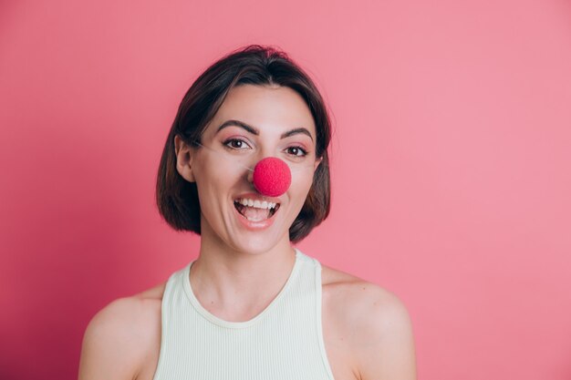 Mujeres sobre fondo rosa mujer joven muy divertida y sonriente con nariz de payaso, humor de fiesta