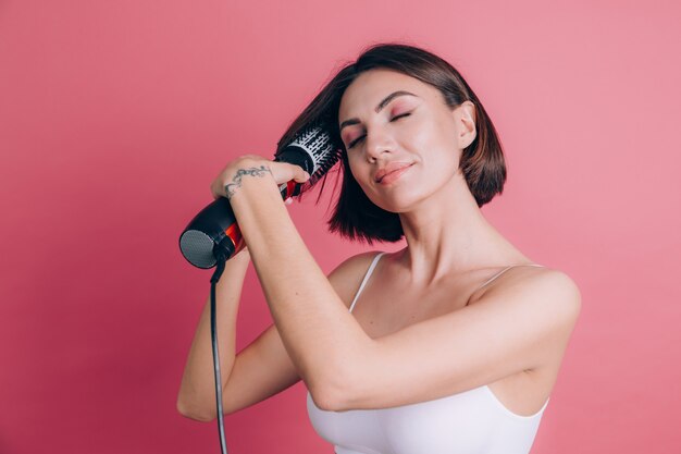 Las mujeres sobre fondo rosa sostienen el secador de pelo con cepillo redondo para peinar el cabello