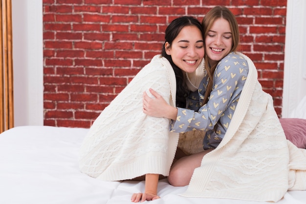 Mujeres sonrientes abrazando y compartiendo una manta