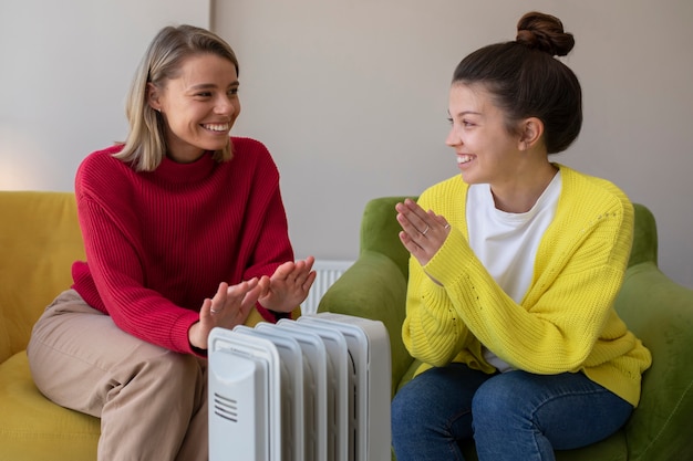 Foto gratuita mujeres sonrientes calentándose cerca del calentador tiro medio