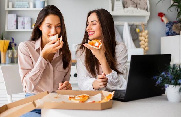 Mujeres sonrientes comiendo pizza después de trabajar