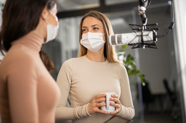 Mujeres sonrientes haciendo radio juntos mientras usan máscaras médicas