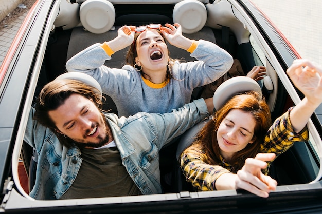 Mujeres sonrientes y hombre positivo divirtiéndose en coche