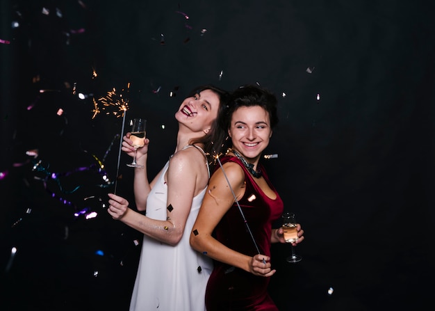 Foto gratuita mujeres sonrientes jovenes que se colocan de espaldas con las luces y los vidrios de bengala