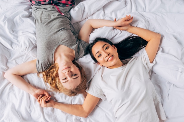 Mujeres sonrientes jovenes que mienten en cama y que llevan a cabo las manos