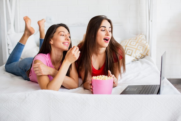 Mujeres sonrientes mirando portátil y comiendo palomitas de maíz