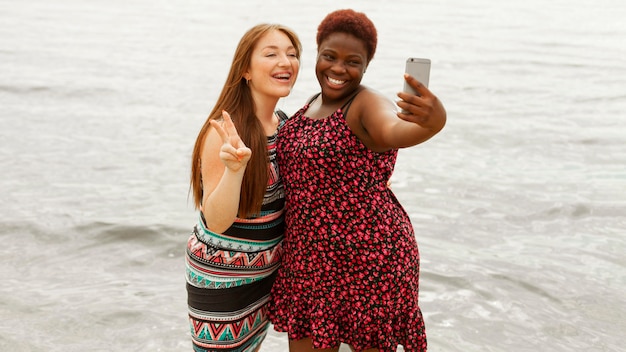 Foto gratuita mujeres sonrientes en la playa tomando selfie