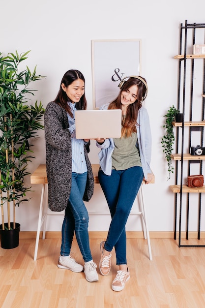 Mujeres sonrientes que se colocan y que usan la computadora portátil junto