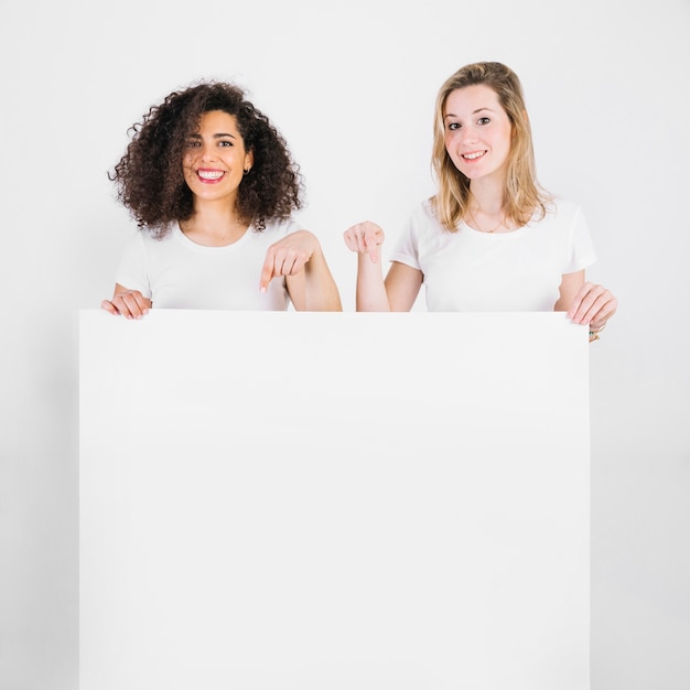 Mujeres sonrientes que señalan en el cartel en blanco