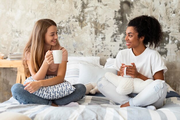 Mujeres sonrientes que tienen una conversación en la cama tomando un café