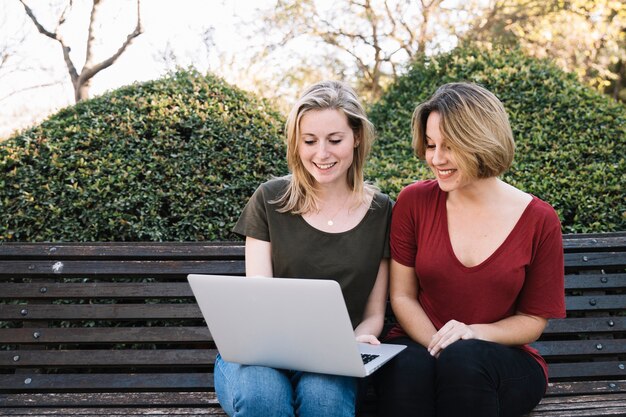 Mujeres sonrientes que usan la computadora portátil en el parque