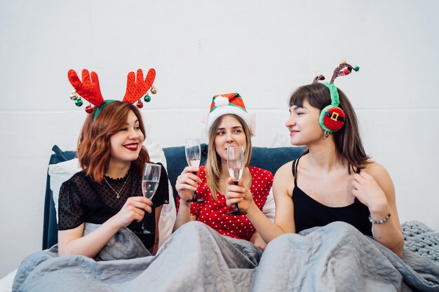 Mujeres sonrientes sosteniendo copas de vino y disfrutando de la fiesta de ppajamas