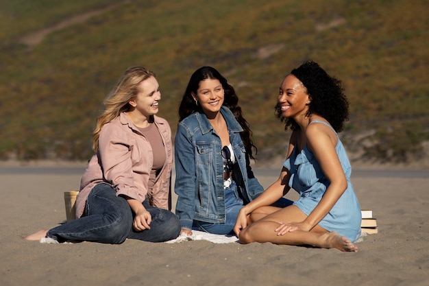 Mujeres sonrientes de tiro completo sentadas en la playa