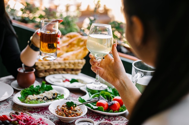 Mujeres sosteniendo copas con limonada en la mesa con diferentes platos