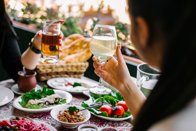 Mujeres sosteniendo copas con limonada en la mesa con diferentes platos