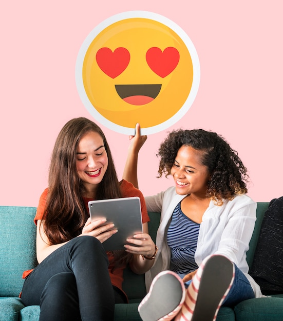 Mujeres sosteniendo un emoticono de ojos de corazón y usando una tableta