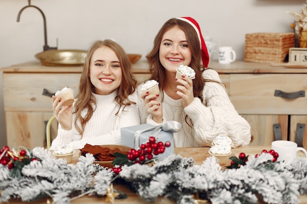 Foto gratuita las mujeres tienen cupcakes. amigos en una decoración navideña. chica con sombrero de santa.