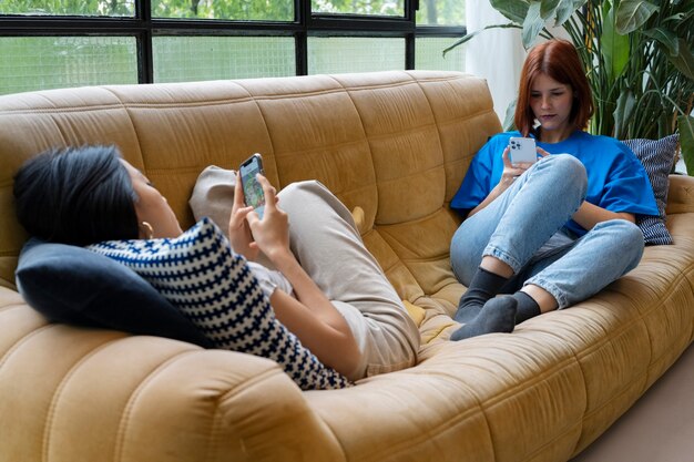 Mujeres de tiro completo acostadas en el sofá con teléfonos inteligentes